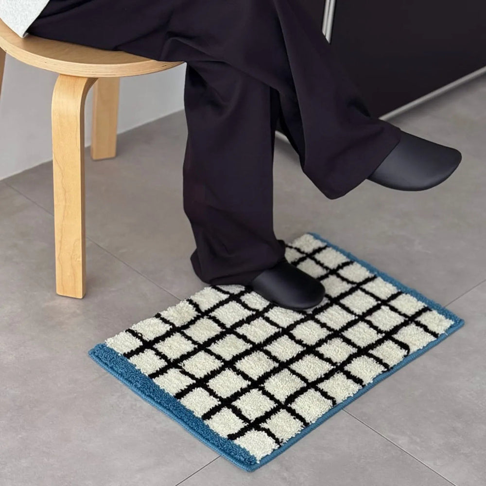 Person sitting on a stool with feet resting on the Plush Grid Checkered Tufted Accent Rug - RoomDen