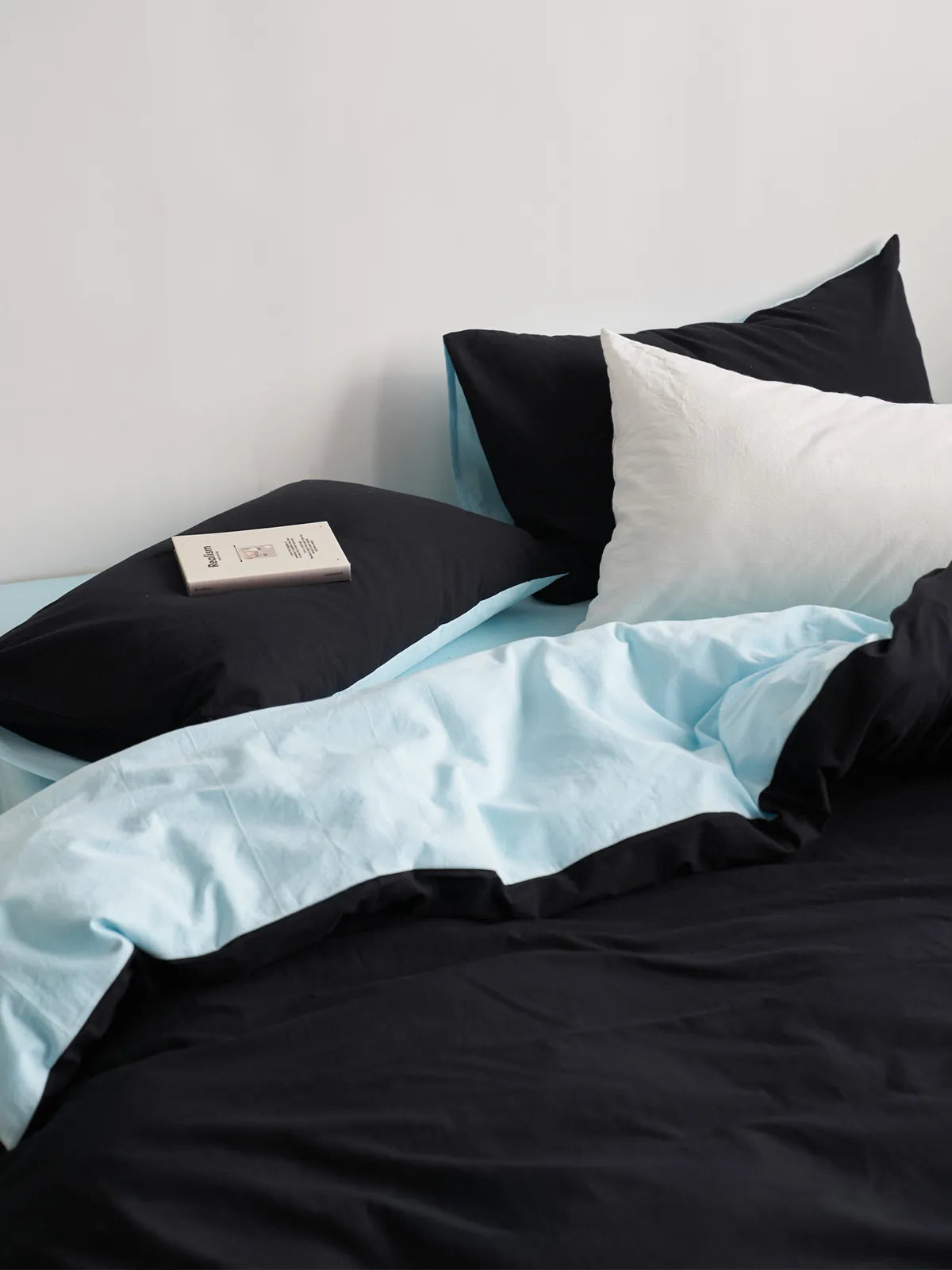 A neatly made bed with the Reversible Two-Tone Washed Cotton Bedding Set, showcasing the black pillows and folded-over cyan duvet. - RoomDen