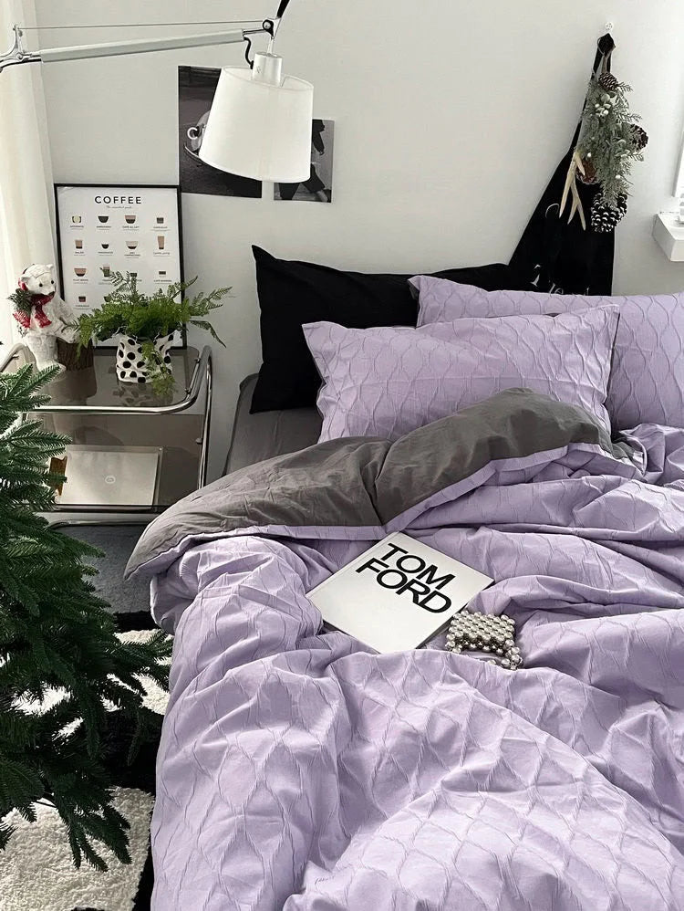 The lavender pintuck duvet cover styled with a grey sheet and a Tom Ford book, showcasing its versatile aesthetic.