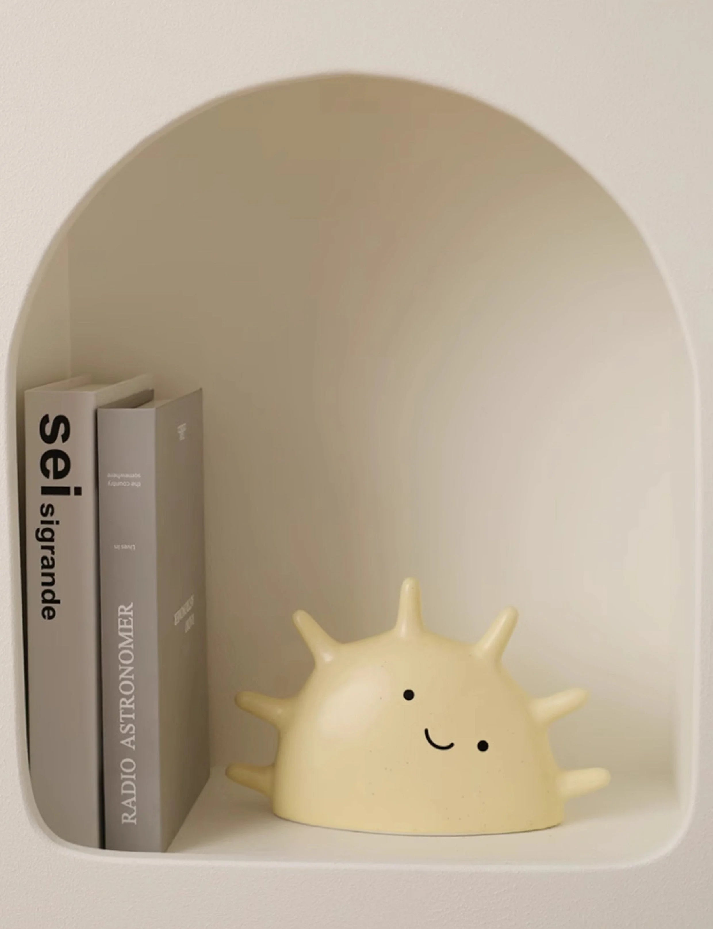 Creamy Beige Smiling Sun Jewelry Organizer sitting in a minimalist white arched wall nook next to books - RoomDen