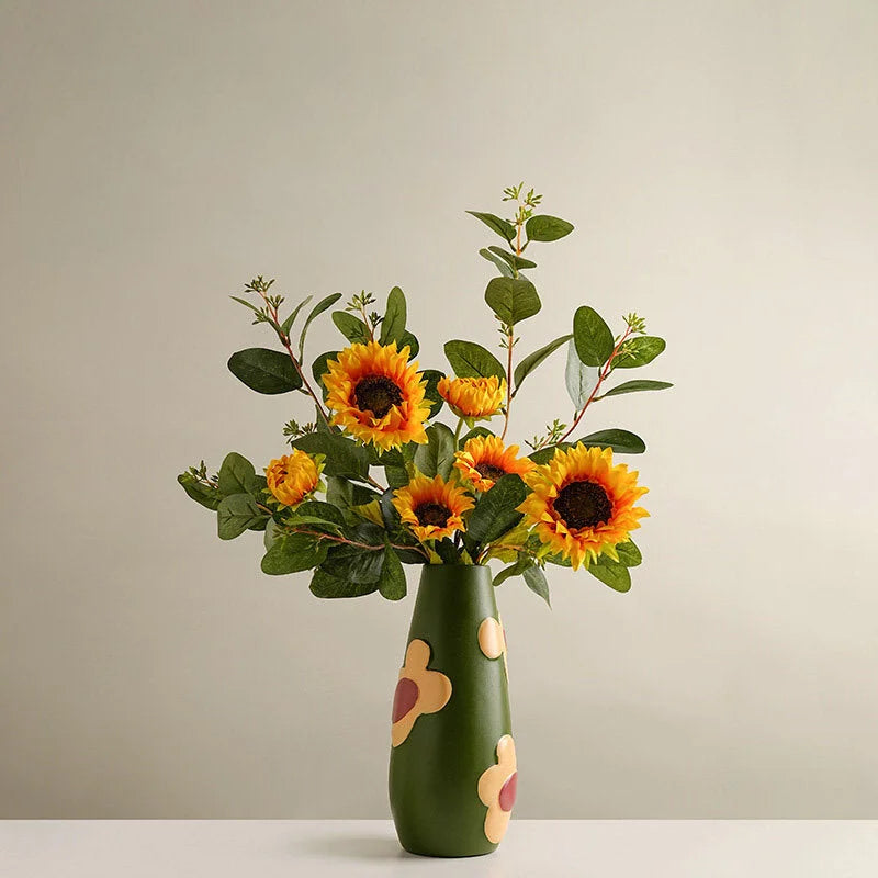 Olive Green Pop Art Floral Ceramic Vase holding a large bouquet of sunflowers on a white table. - RoomDen