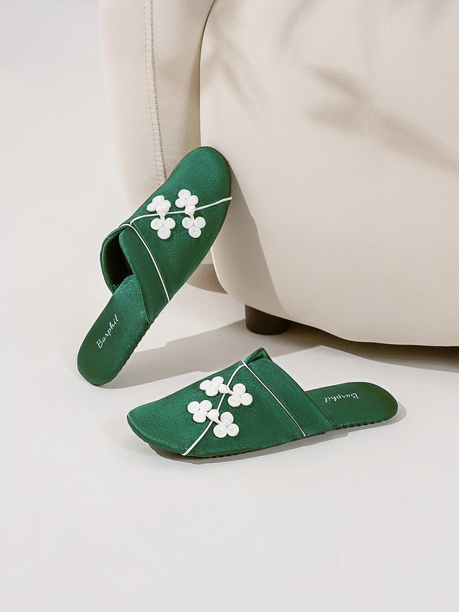 Green satin slippers leaning against a beige sofa showing side profile and embroidery - RoomDen