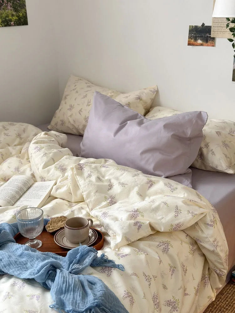 A breakfast tray with a cup and book resting on the soft, crinkled wisteria floral duvet cover - RoomDen.