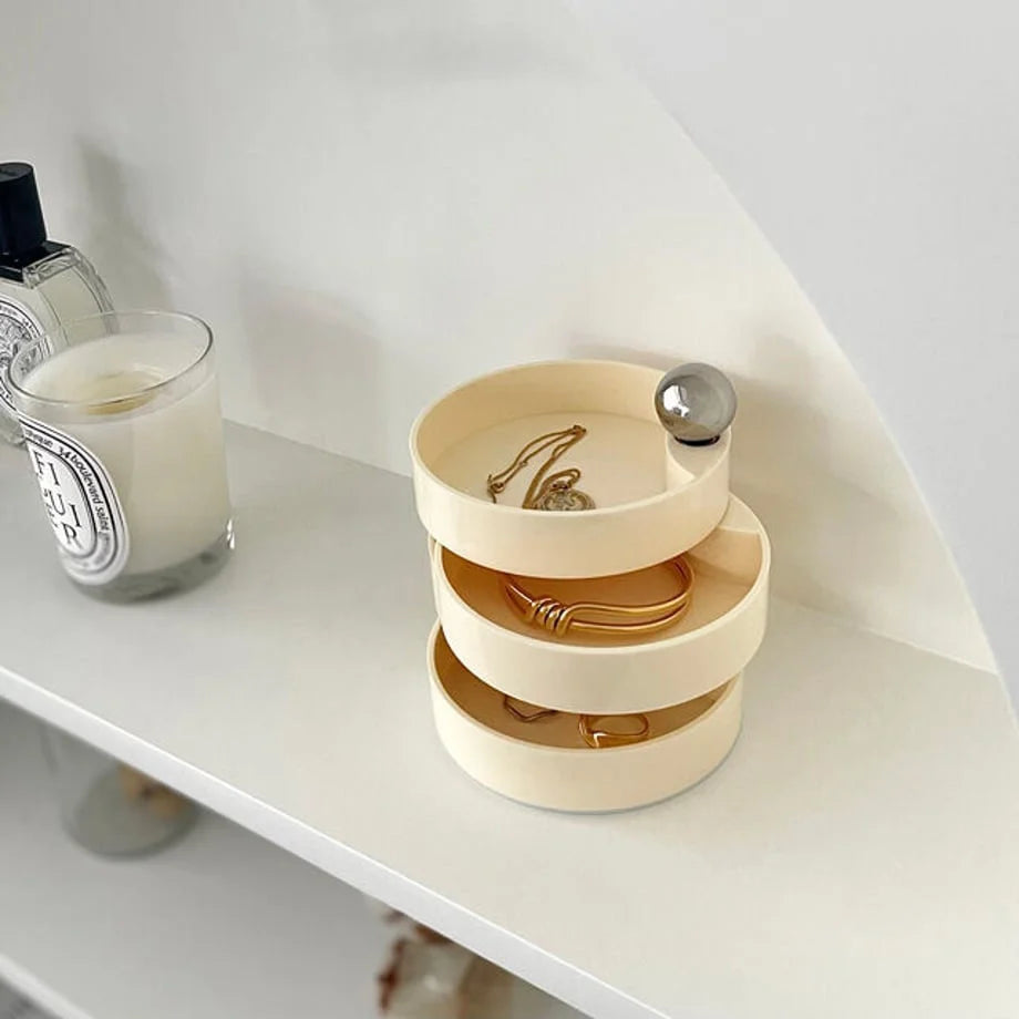 The Creamy Beige rotating jewelry box on a white shelf, partially open showing necklaces and bracelets. - RoomDen