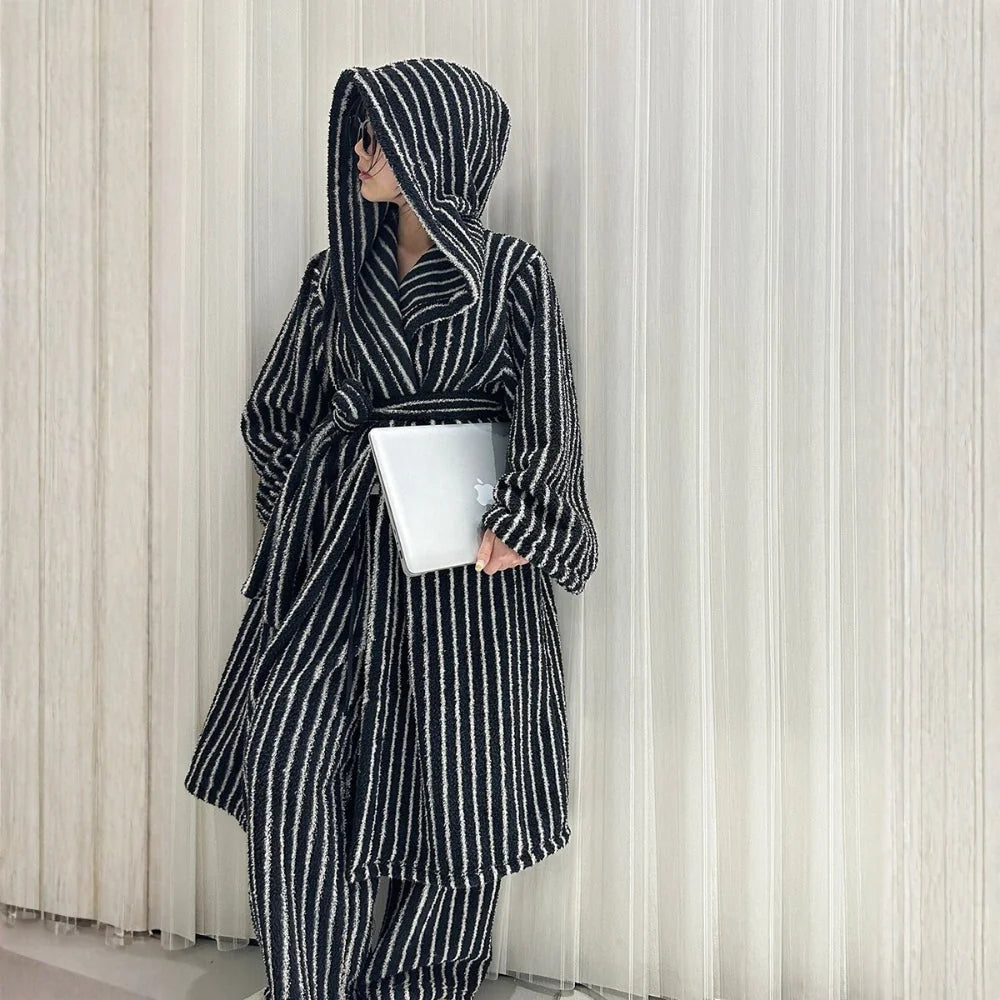Full body shot of a model in a black and white striped flannel fleece robe and pants set, holding a laptop against a white curtain backdrop - RoomDen.