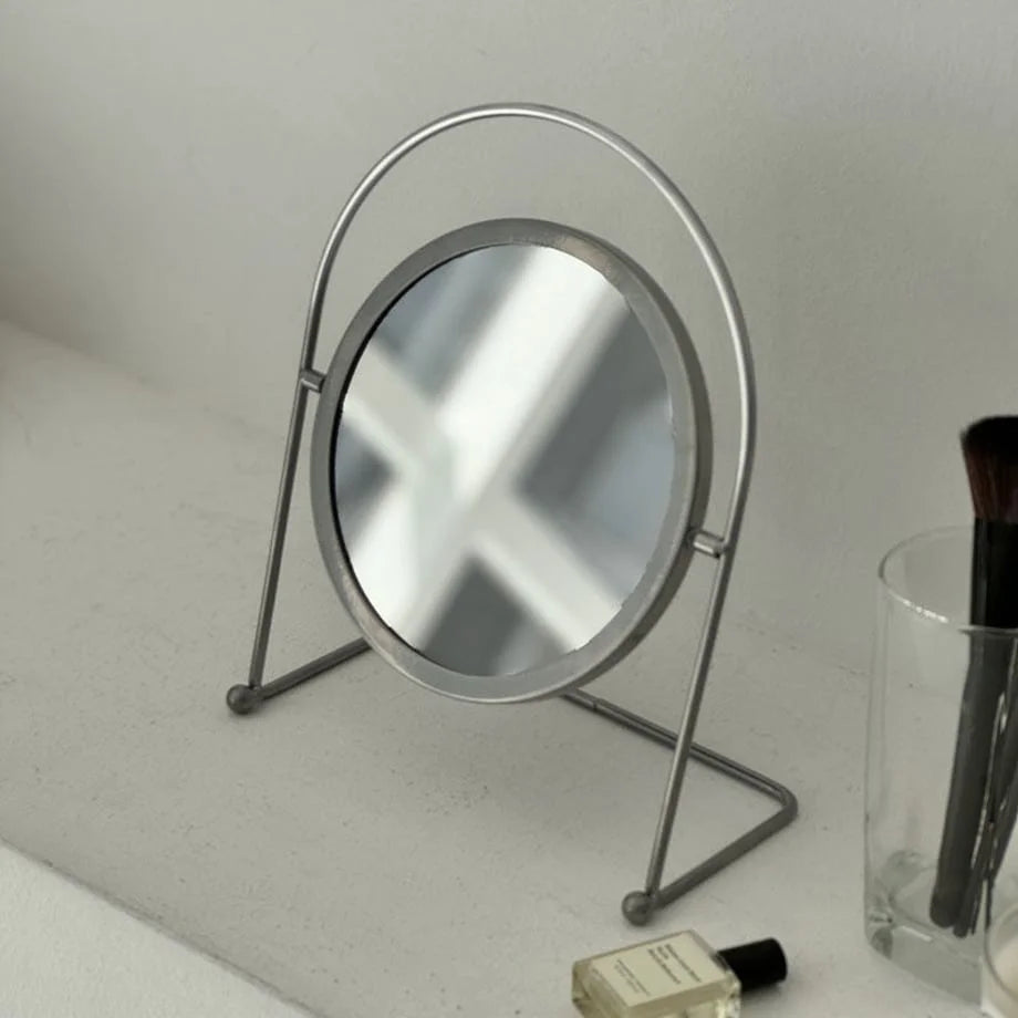 Close-up of the matte grey metal swivel desktop mirror on a white shelf. - RoomDen