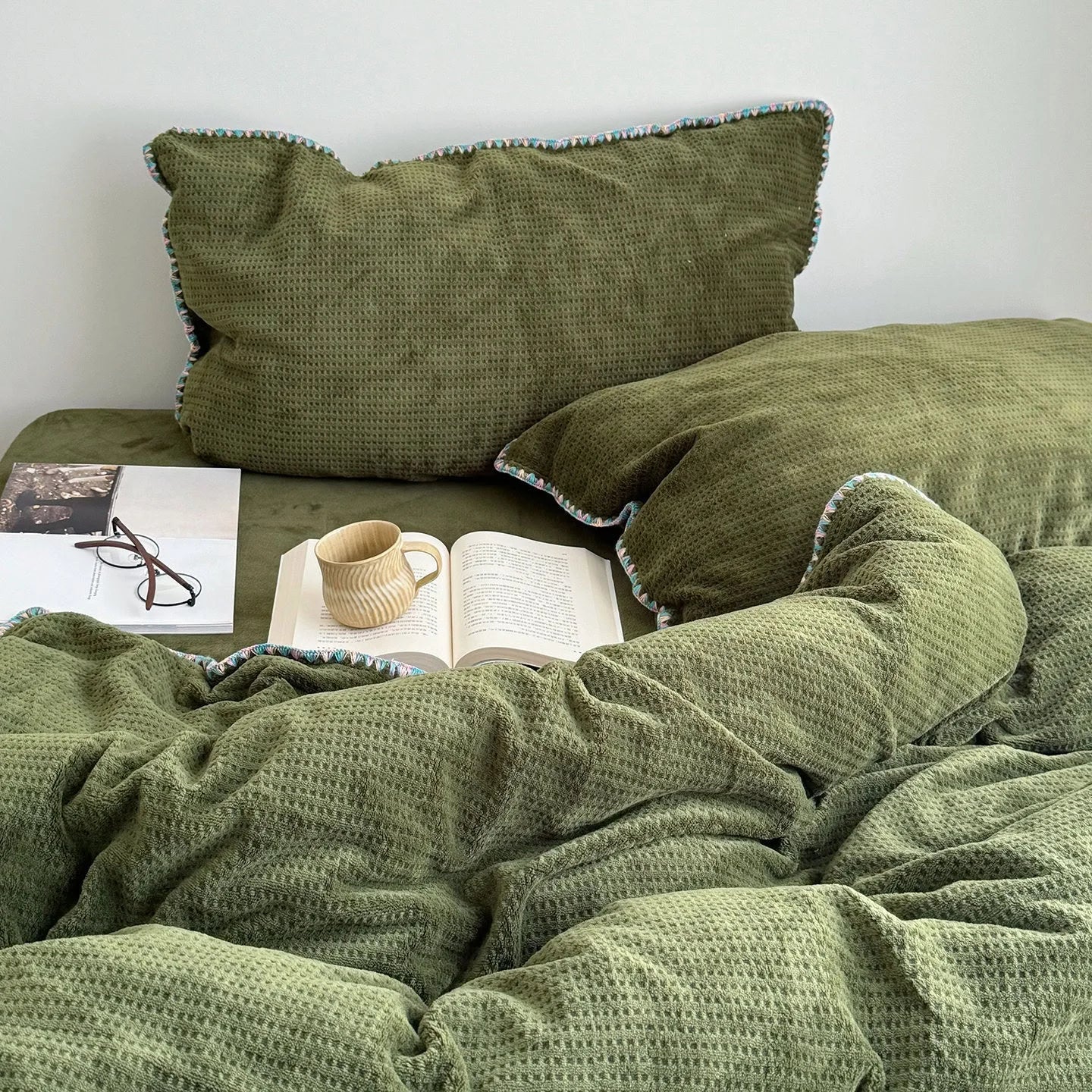 Open book and coffee mug resting on the Olive Green Waffle Fleece Bedding Set.