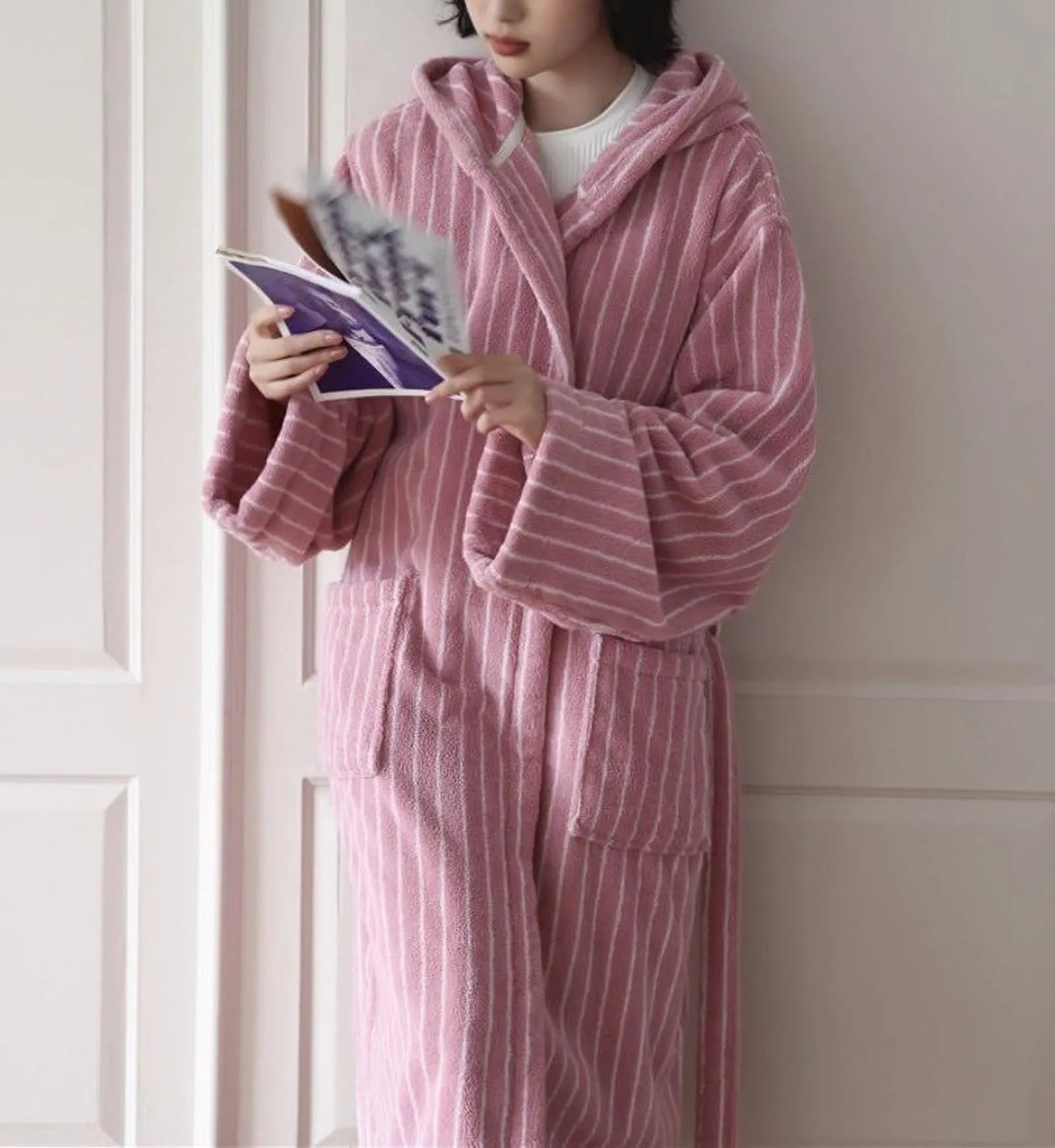 Woman standing wearing a plush pink vertical striped hooded robe reading a magazine - RoomDen