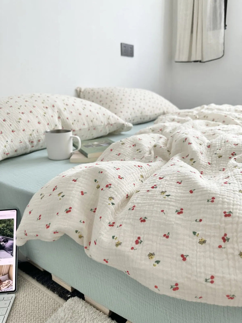 A cozy bed with a textured white washed cotton bedding set featuring a cherry and bee print, styled with a mug and laptop. - RoomDen