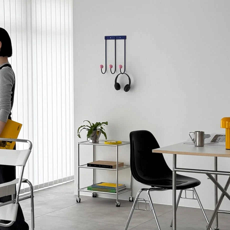 A minimalist room with the Blue & Pink Metal Wall Hooks mounted on a white wall above a silver rolling cart. - RoomDen