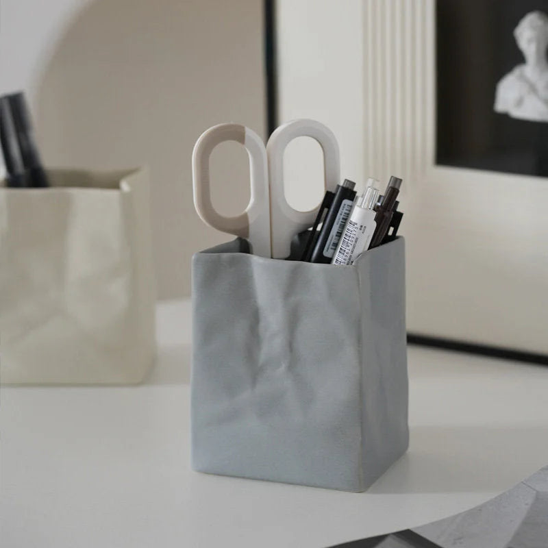 An ash grey crumpled ceramic organizer holding pens, next to a cream one on a minimalist desk. - RoomDen