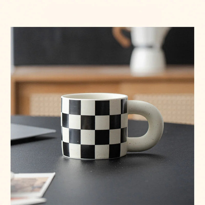 The Black Checkered Ceramic Mug with a Puffy Handle on a modern black desk. - RoomDen