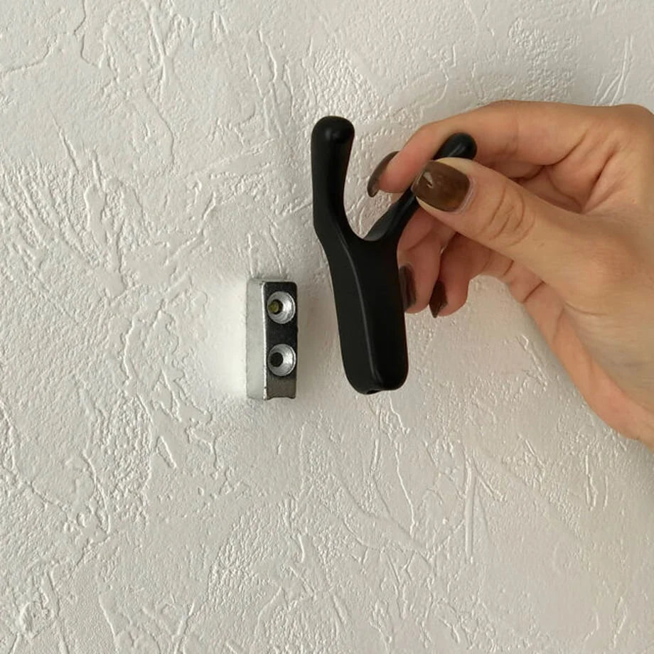 A hand holding the black branch-shaped hook next to the silver mounting plate on the wall to show installation - RoomDen