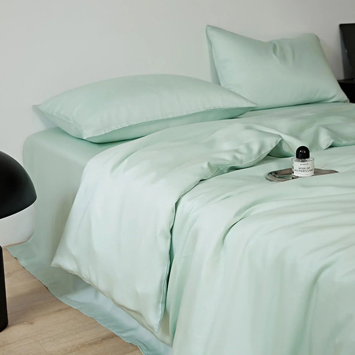 The Mint Green bedding set styled on a bed next to a modern black lamp.