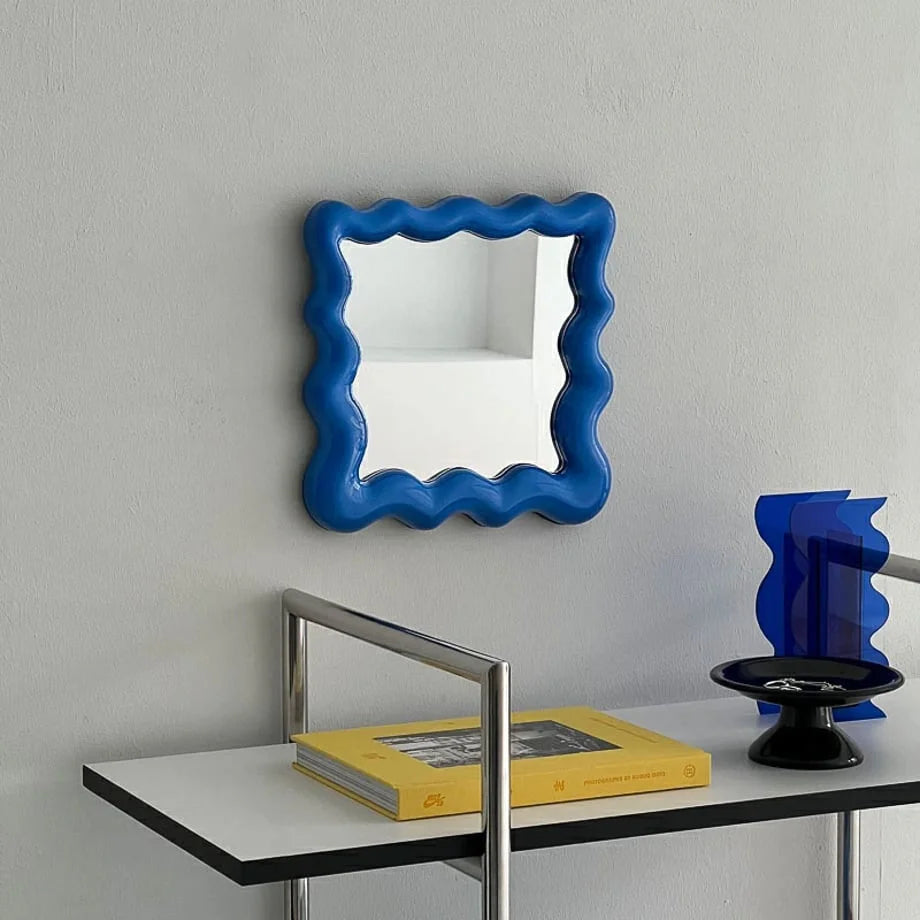 Glossy blue wavy frame desktop mirror hanging on a light grey wall above a console table - RoomDen