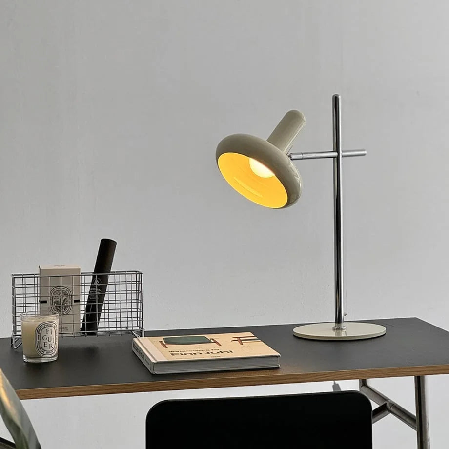 The Sculptural Metal Accent Lamp turned on, casting a warm yellow light on a desk - RoomDen.