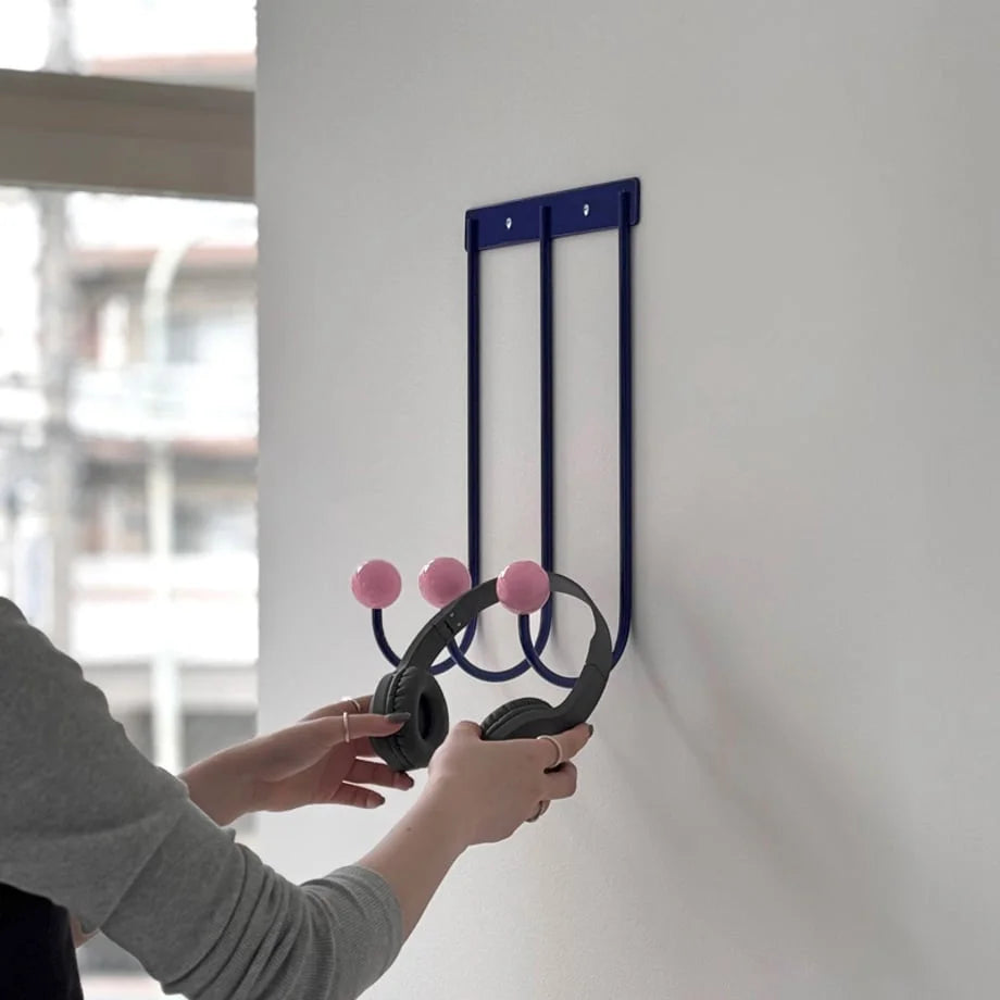 Close-up of the Blue & Pink Color Block Metal Wall Hooks holding black headphones. - RoomDen