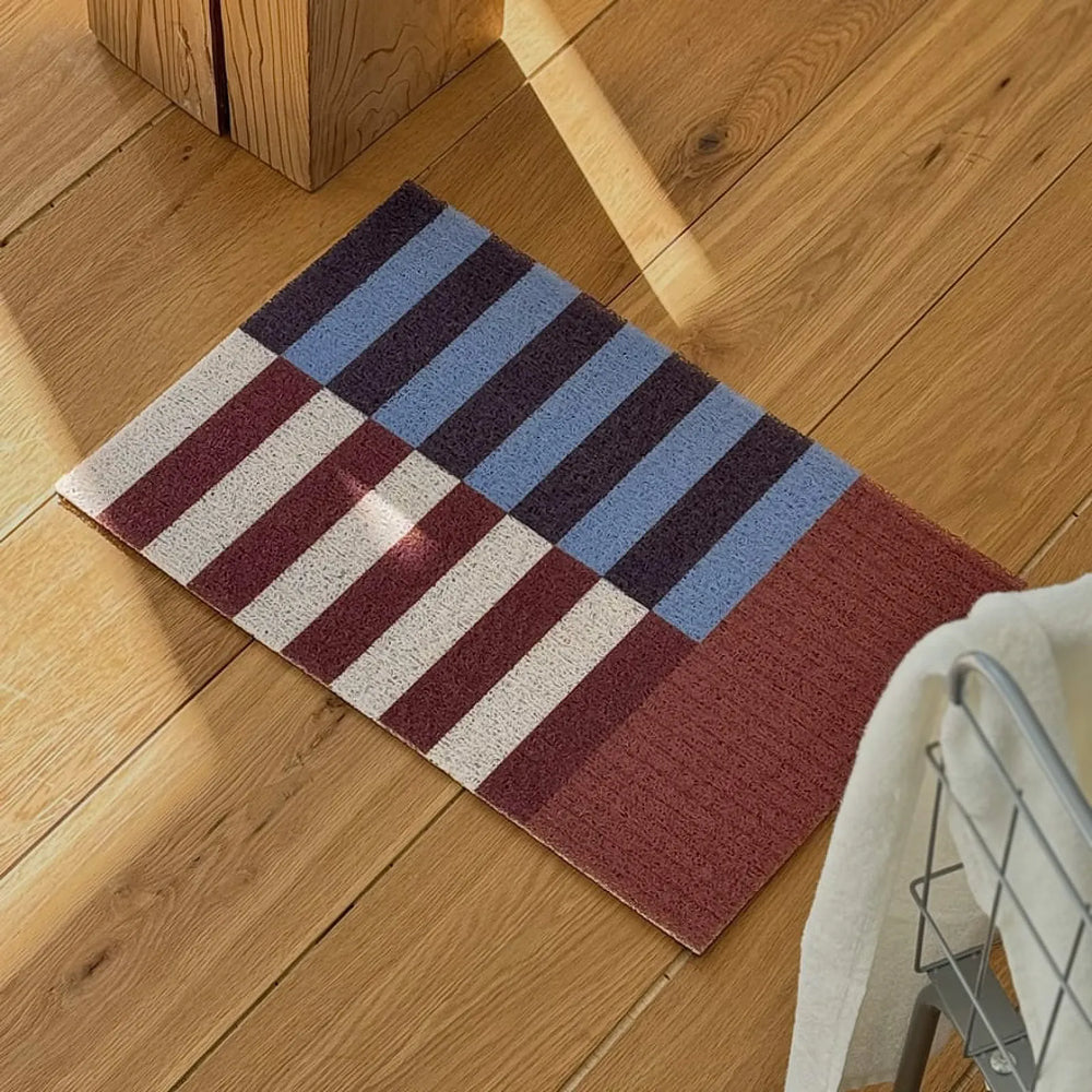 Bauhaus style rust and blue geometric PVC coil doormat on wooden floor - RoomDen