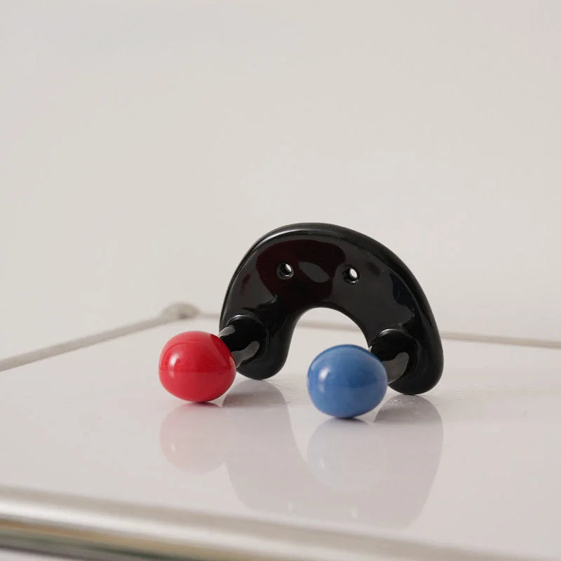 Close-up of a black U-shaped ceramic wall hook with one red and one blue ball - RoomDen.