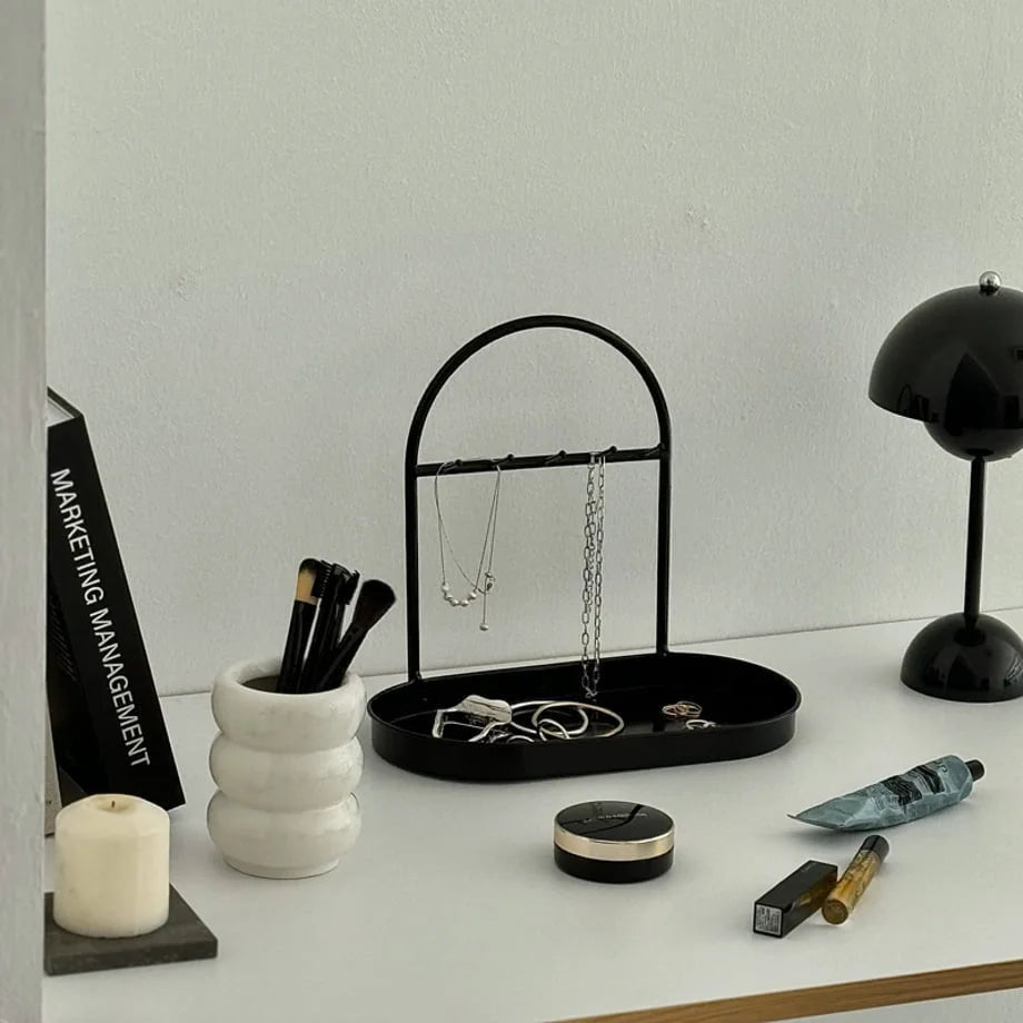 Black Sleek Arched Metal Jewelry Organizer on a white desk with beauty products. - RoomDen