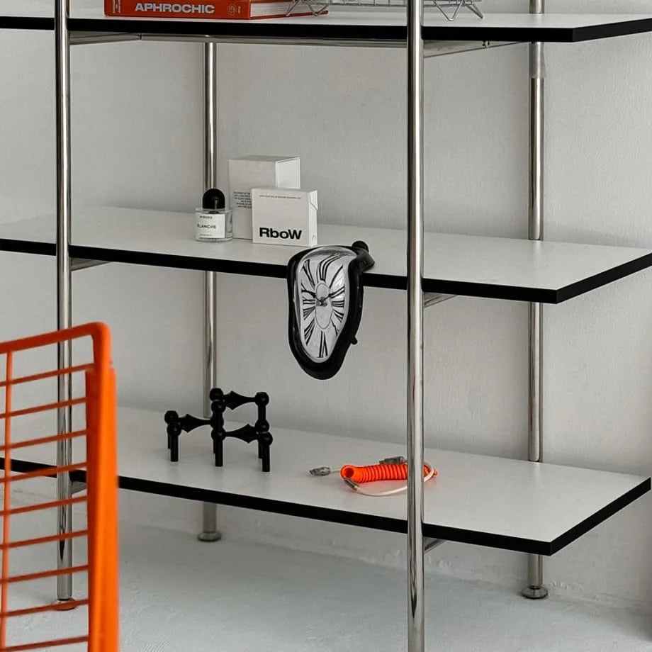 Wide view of the black melting clock on a modern shelving unit with other decor.