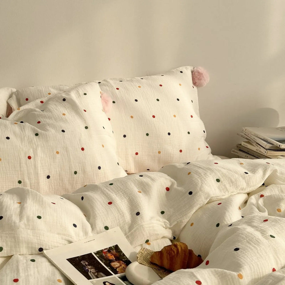 A close-up of a soft white washed cotton bedding set with colorful polka dots and a cute pink pom-pom on the pillow. - RoomDen