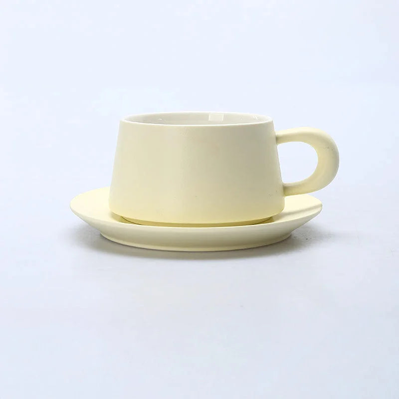 A Cream Beige matte ceramic coffee cup with a chunky handle and matching saucer on a white background. - RoomDen