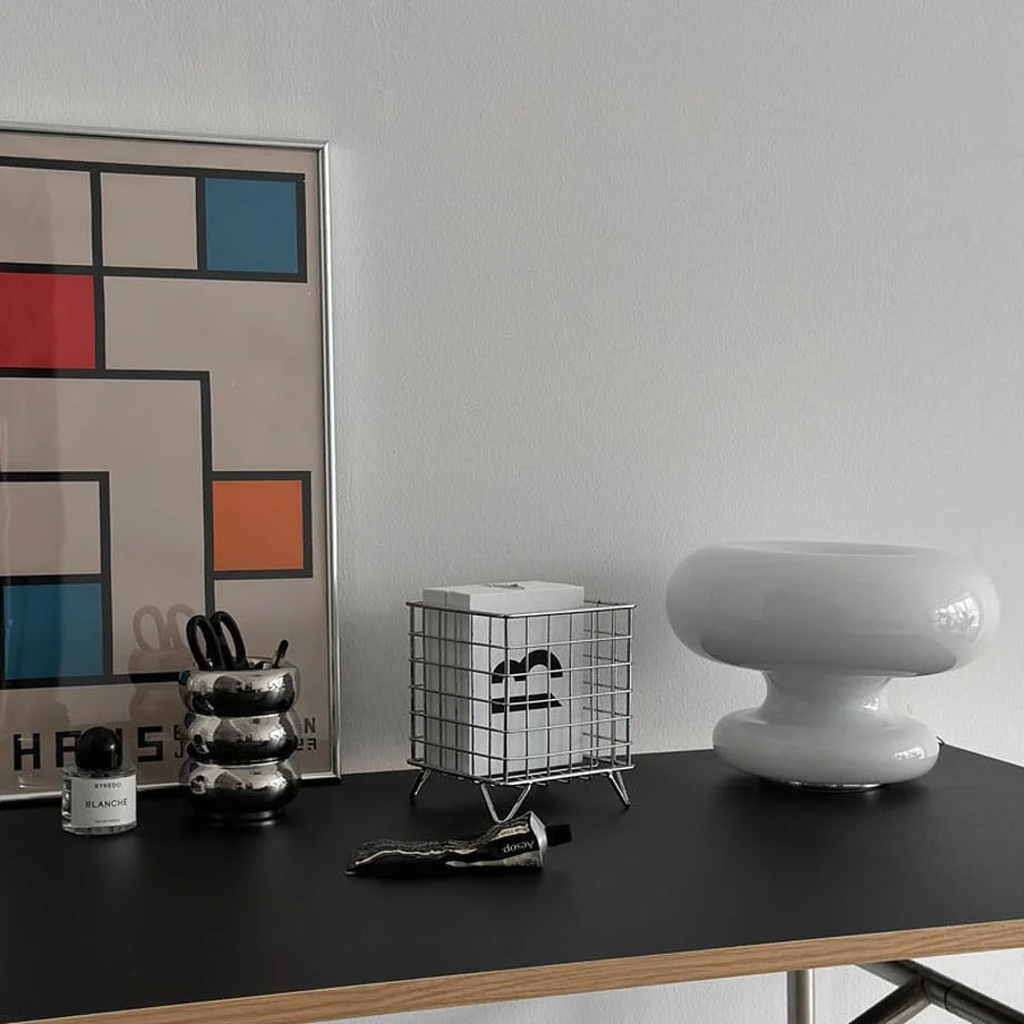 Wide view of a chrome metal storage basket on a modern desk with a white mushroom lamp and Bauhaus art print - RoomDen.