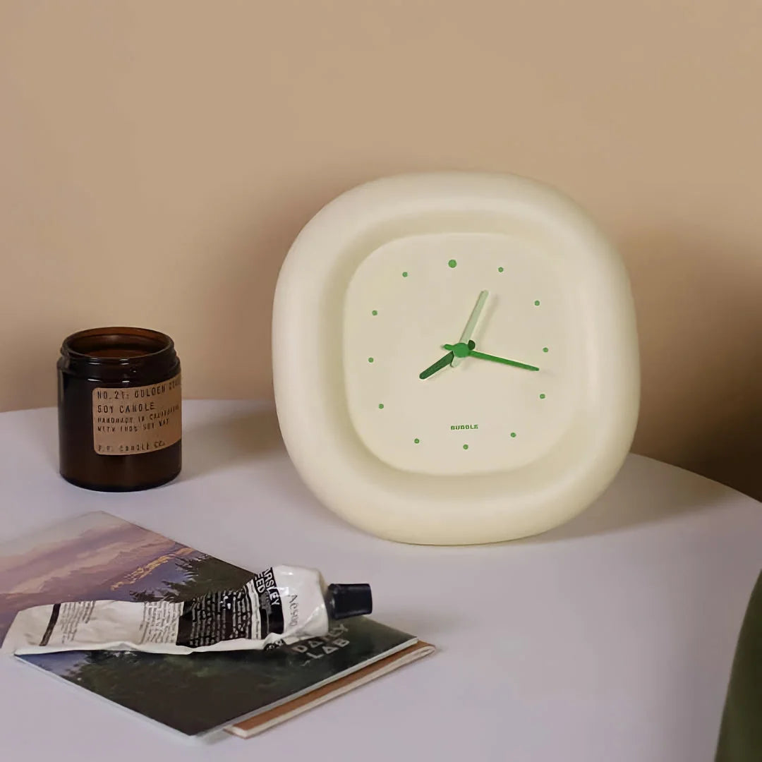 The Creamy Beige Puffy Bubble Table Clock on a white bedside table next to a candle and books - RoomDen