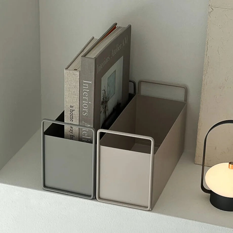 Two minimalist metal desktop organizers, one slate grey and one warm beige, holding books on a white shelf. - RoomDen