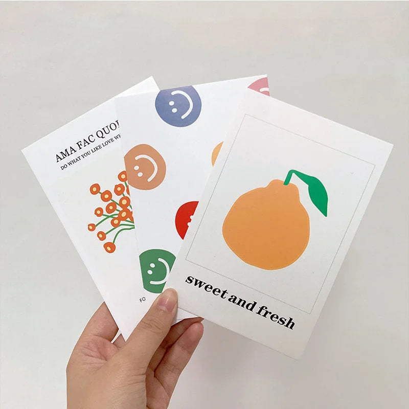 A hand holding three cards from the Colorful Doodle Wall Collage Kit, showing a pear design and smiley faces.