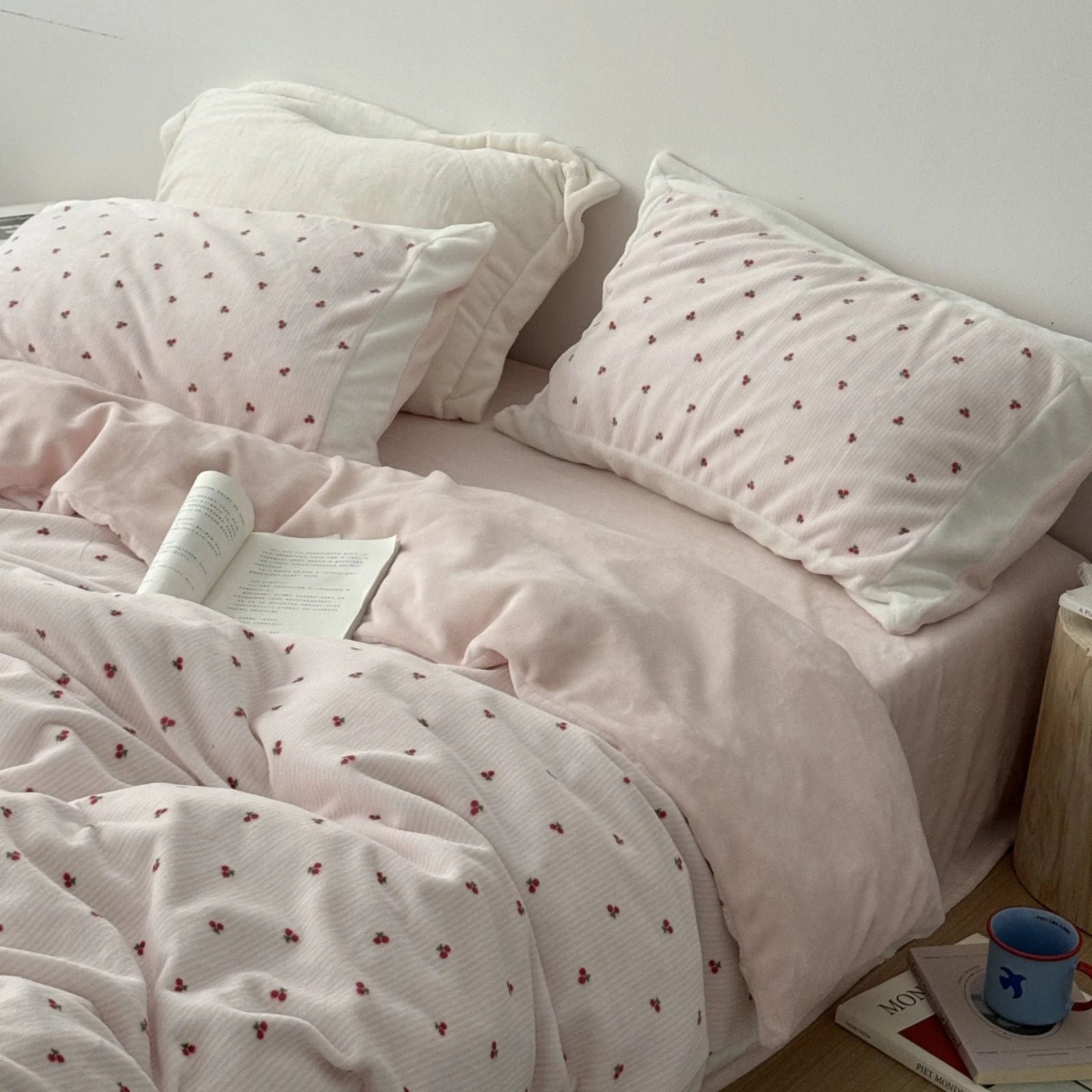 Plush pink flannel fleece bedding set with embroidered cherries, styled on a bed with an open book. - RoomDen