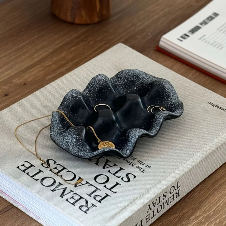 The Black Speckled Wavy Ceramic Jewelry Dish holding jewelry, sitting on a book.