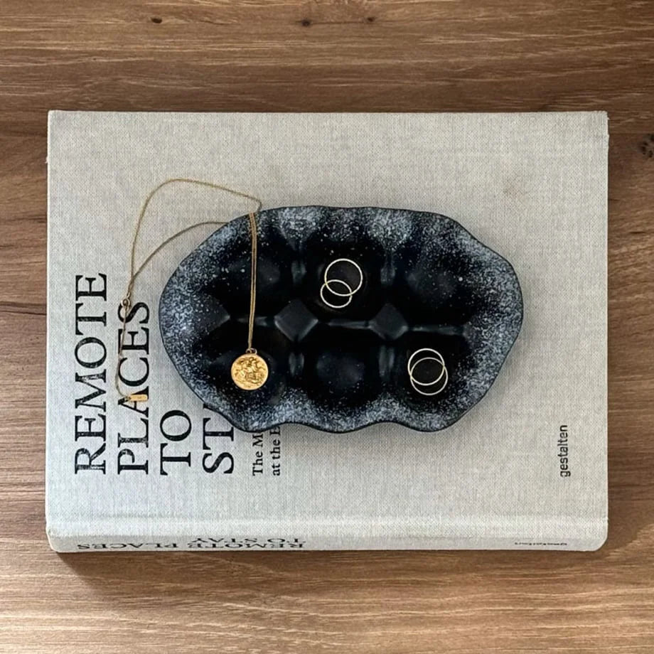 Top-down view of the Black Speckled Wavy Ceramic Trinket Tray holding gold rings and a necklace.