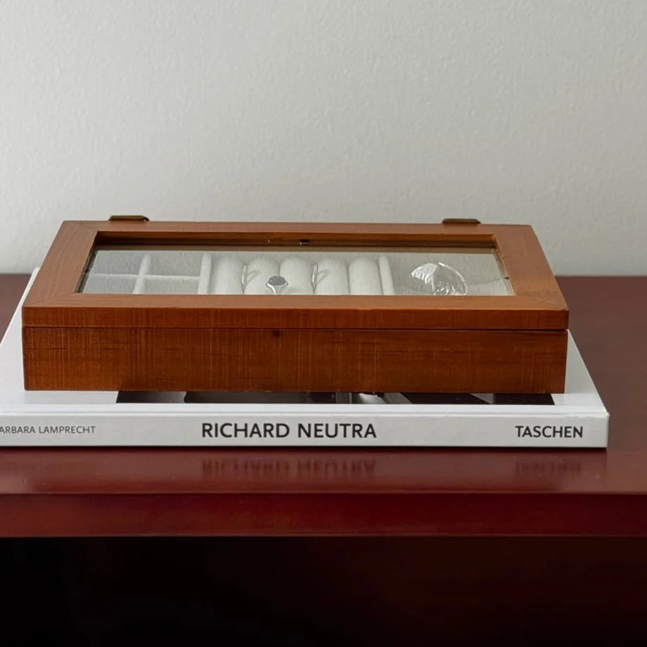 The closed wood jewelry organizer with its glass lid, sitting on top of a design book.