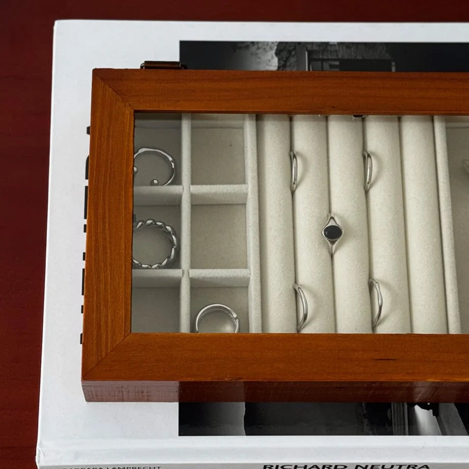 An overhead close-up view through the glass lid of the wood jewelry organizer, showing silver rings neatly arranged.