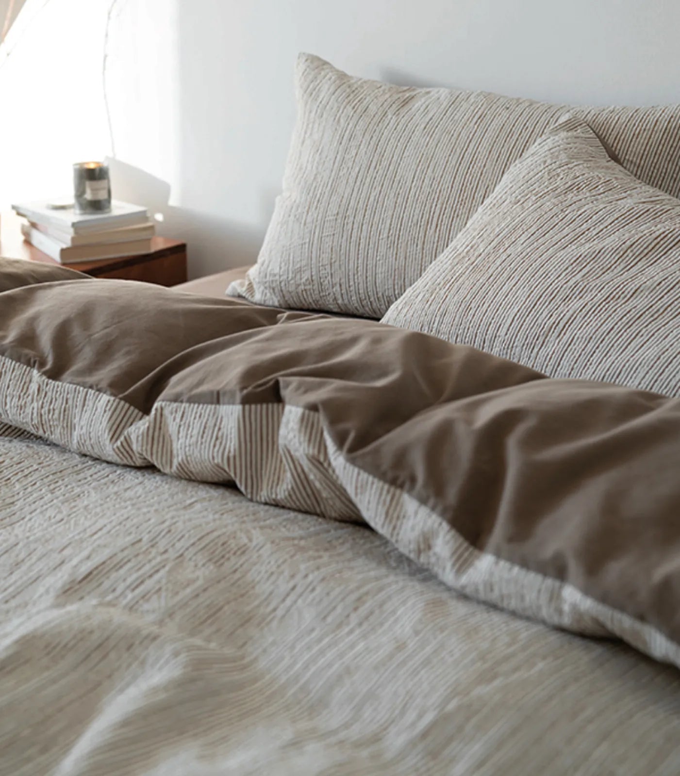 Side view of the Latte Brown pinstripe bedding showing the solid brown reverse side, with a candle on the nightstand.