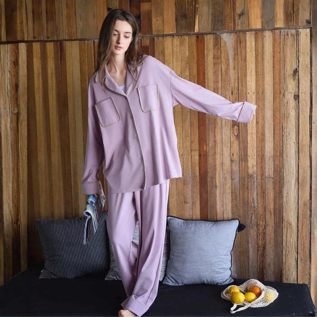 Full body shot of a model standing in the lavender cotton pajama set against a wooden wall. - RoomDen