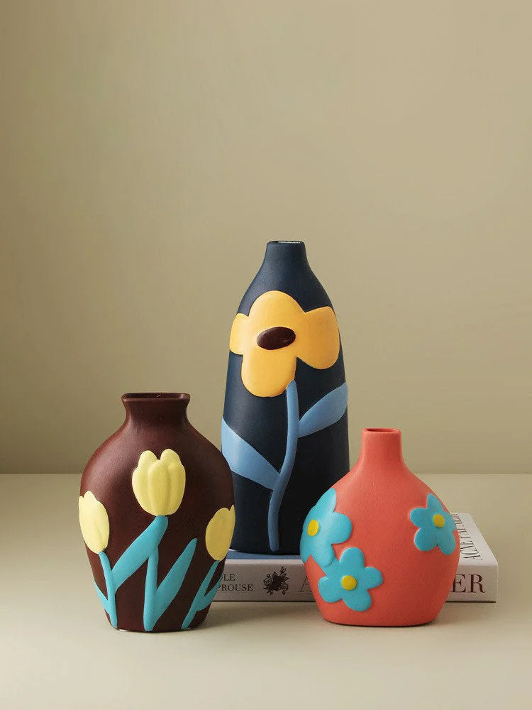 Three floral ceramic vases in brown, navy, and coral grouped together on a neutral surface with books. - RoomDen
