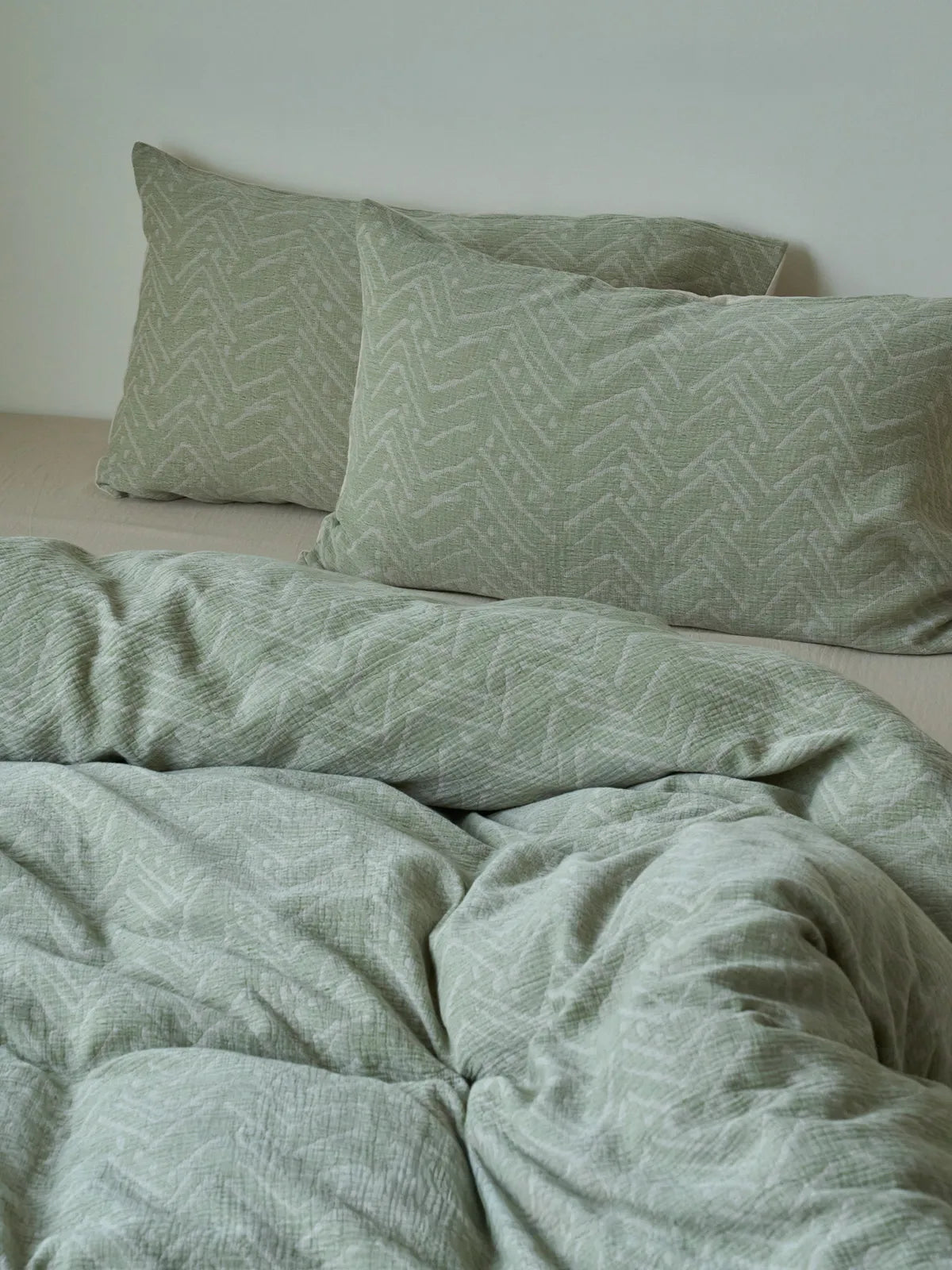 Soft Crinkled Geometric Washed Cotton Bedding Set in sage green, showing the duvet and two pillows on a bed. - RoomDen