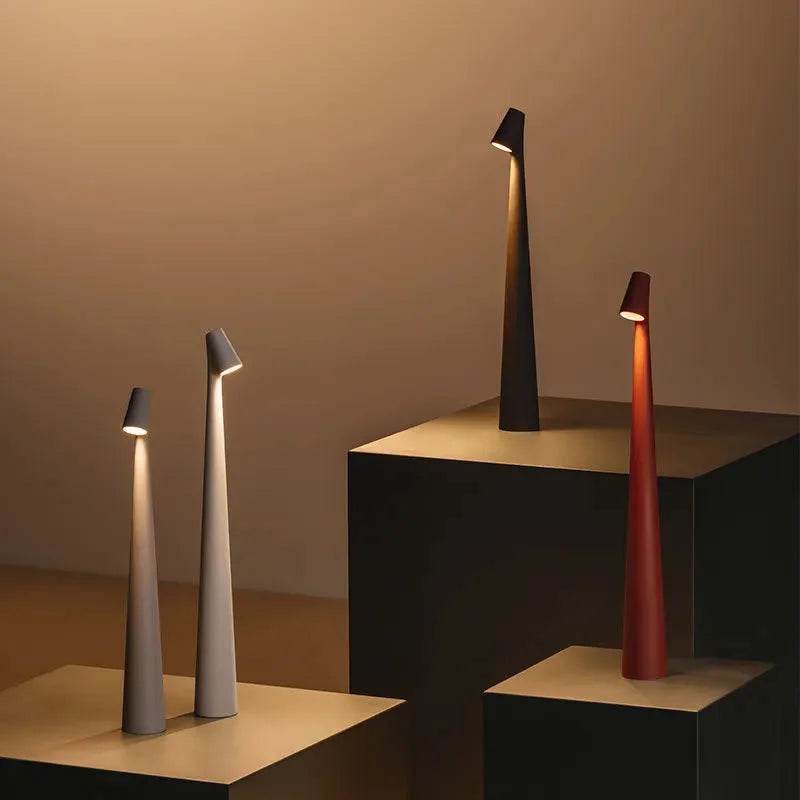 A collection of four cordless touch lamps in taupe grey, matte black, and terracotta red, displayed on geometric blocks - RoomDen.