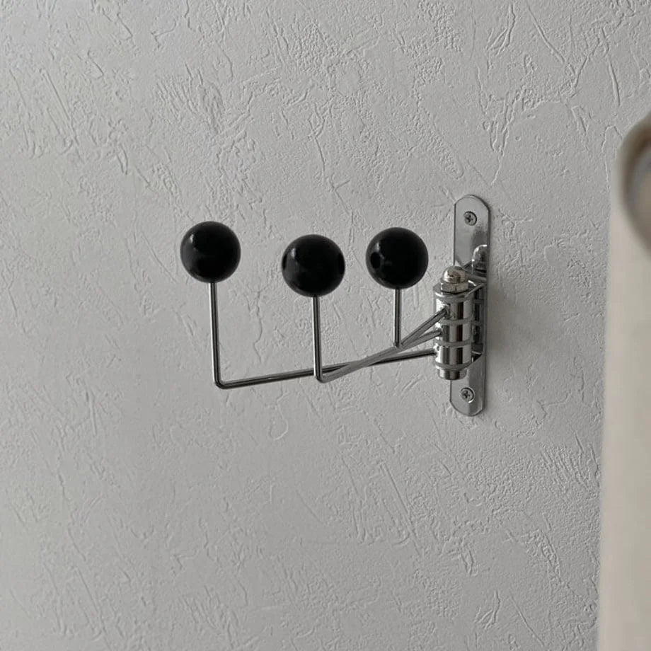 Close-up of the Smooth Ball-End Swivel Metal Wall Hook in Black on a textured white wall - RoomDen.