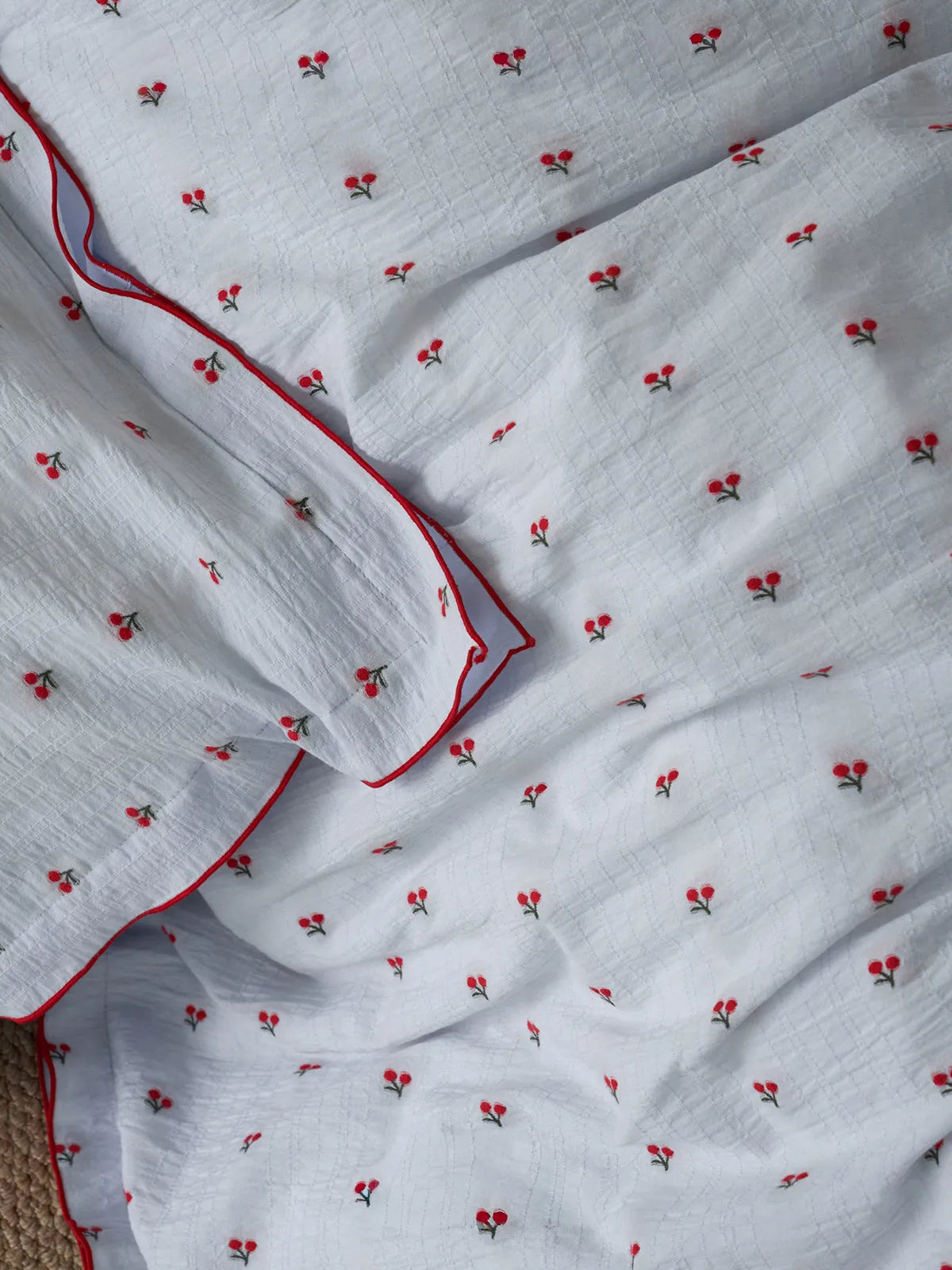 Texture detail shot of crinkled white cotton fabric with red embroidered cherries RoomDen.