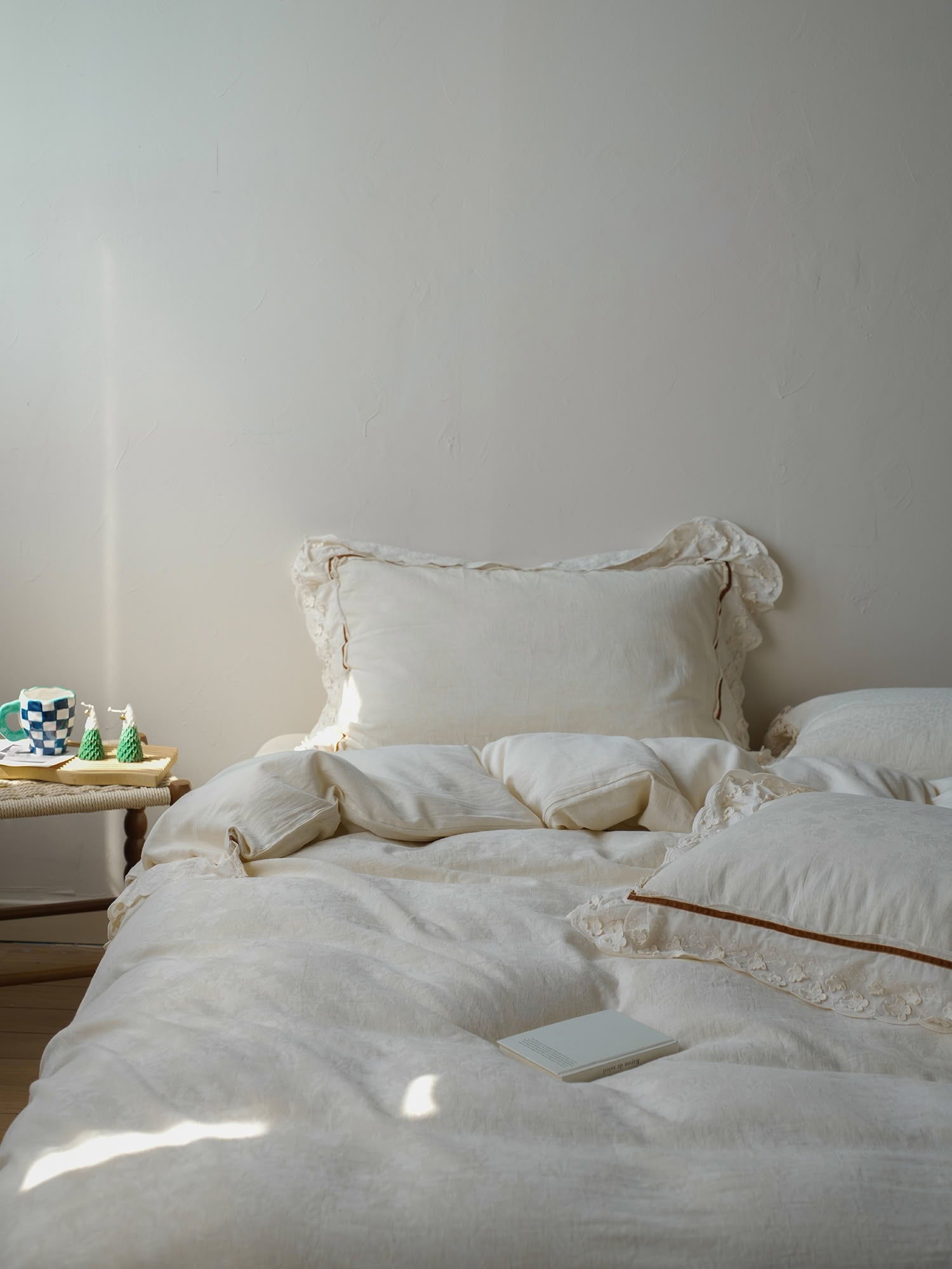 Neutral cream linen bed styling with soft lace pillows and relaxed drape – RoomDen