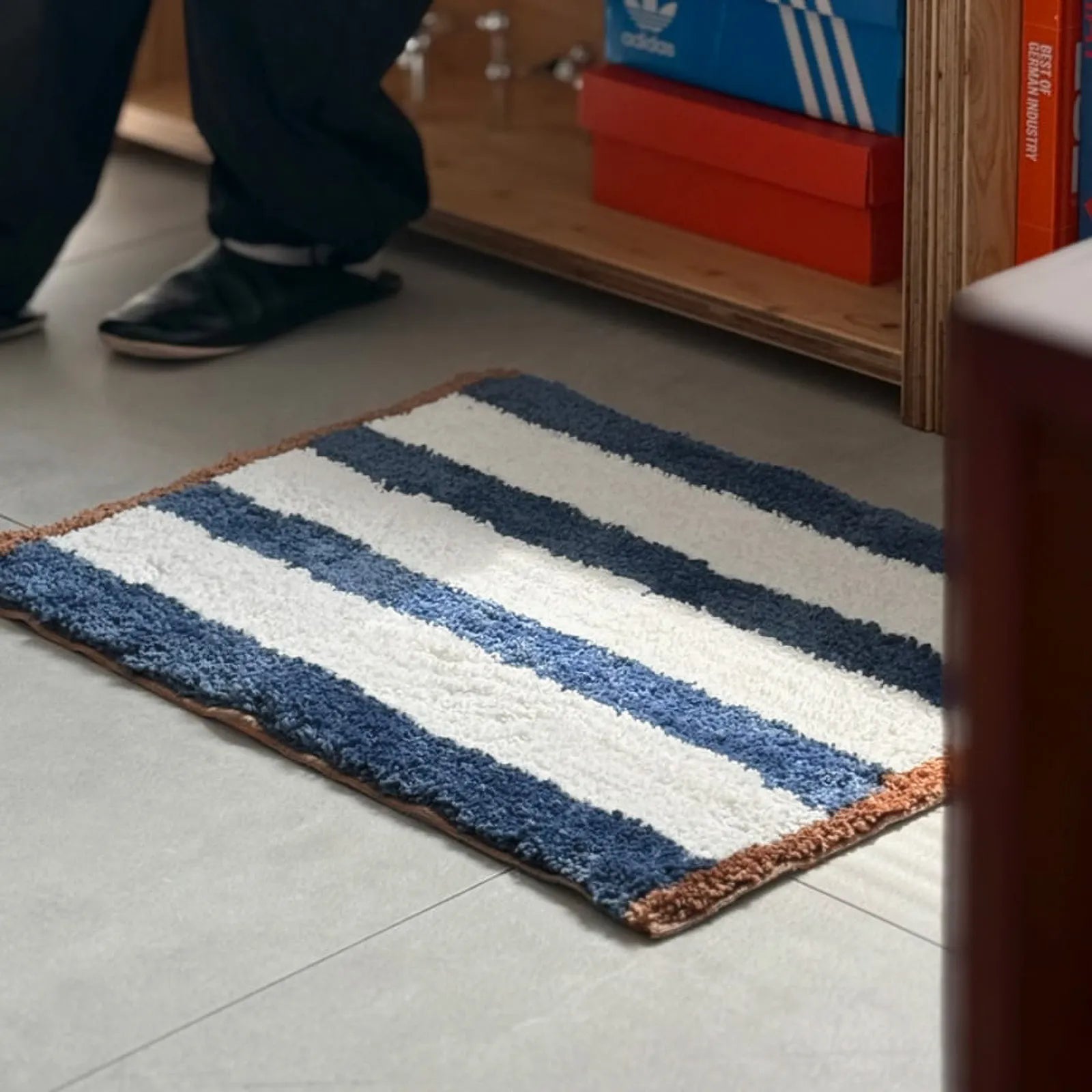 Blue and white striped shaggy accent rug with brown trim on grey tile floor - RoomDen