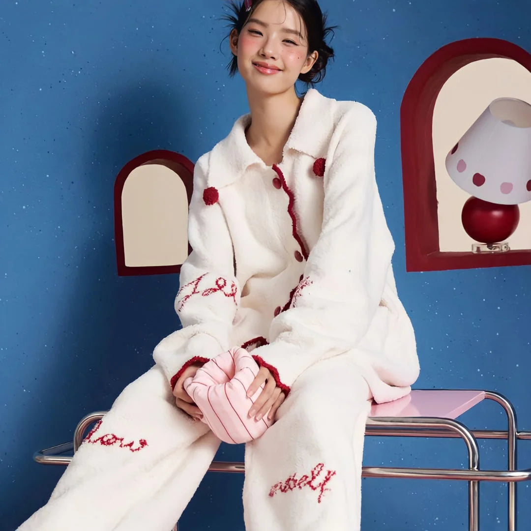 Model sitting playfully in the Cream White pom-pom fleece pajama set against a blue background. - RoomDen