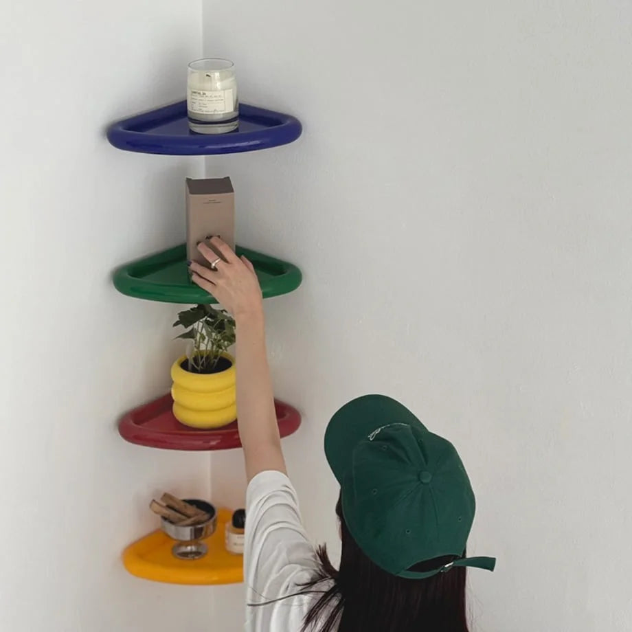 A hand reaching for a box on a green Chunky Curved Corner Shelf, part of a colorful four-shelf wall display. - RoomDen