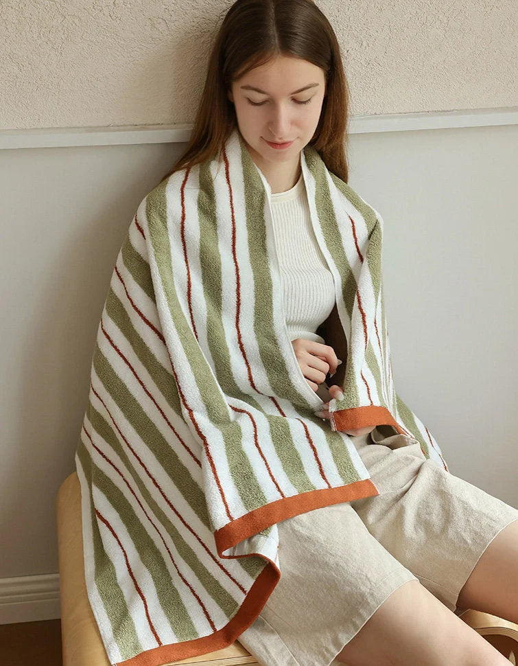 A woman wrapped in the large striped cotton bath towel, sitting in a cozy, minimalist setting - RoomDen