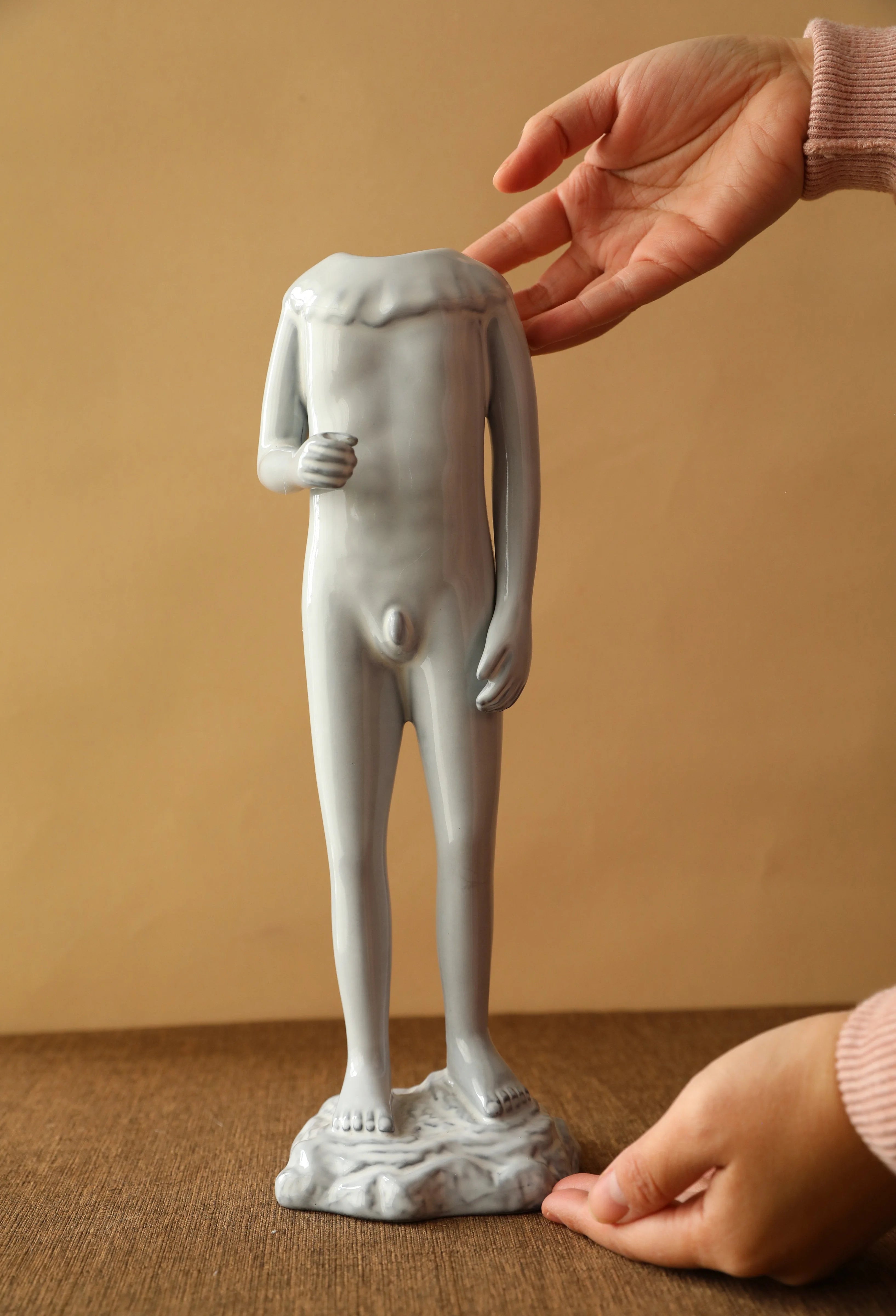 Hand positioning the male figure ceramic vase on a dark wood surface. - RoomDen