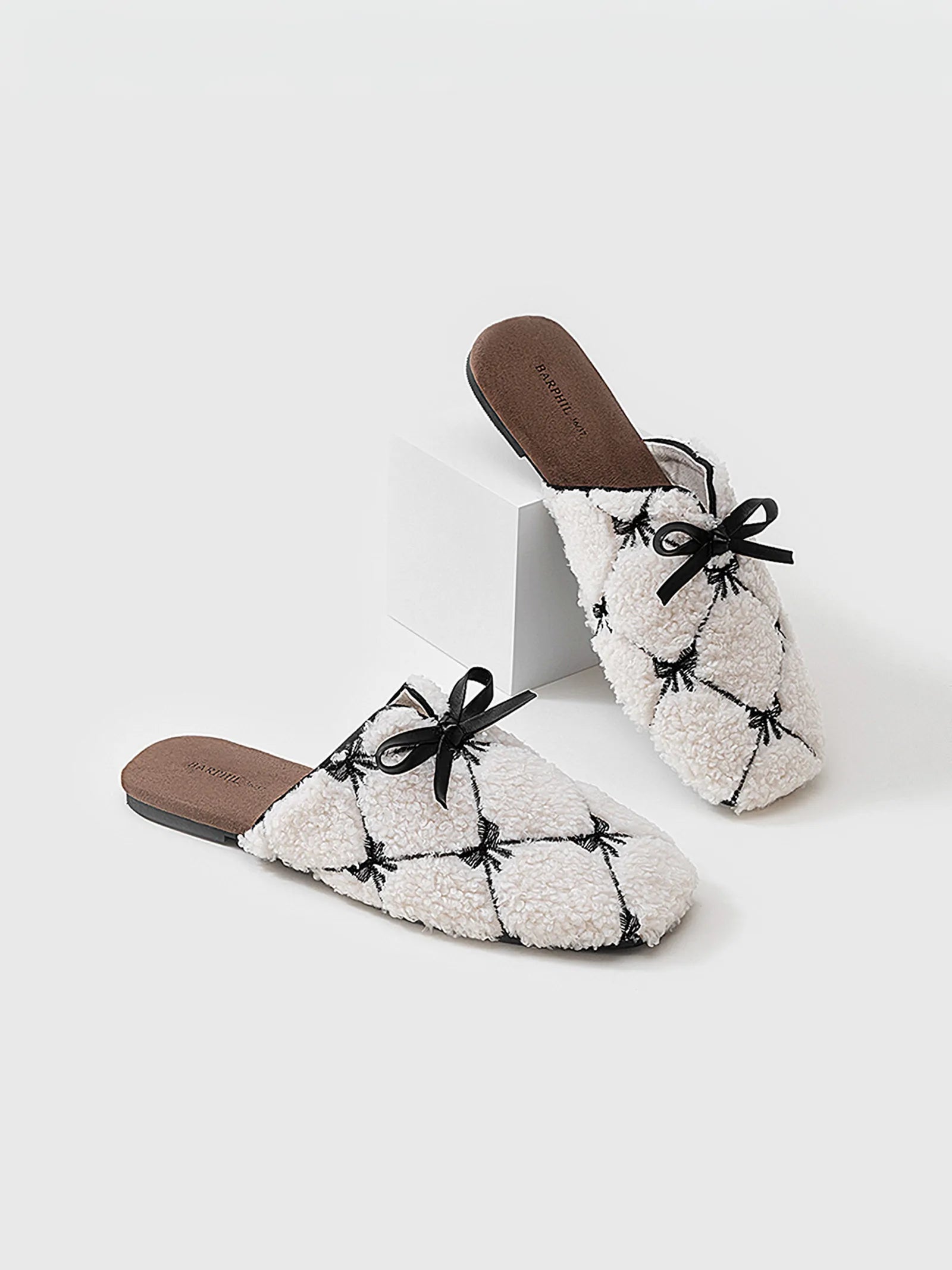 Close up of fuzzy white slippers featuring black bow tie on white block